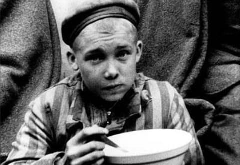 After Liberation, A Child in a Prisoner’s Uniform Eating His First Meal, Dachau, Germany