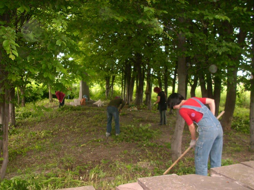 Student volunteers working with the pastor Alexei Radchuk to removing  overgrowth from the path connecting the two monuments at the memorial site.